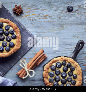 Piatto di laici mirtillo deliziosi pasticcini con crema alla vaniglia crema sulla luce di legno rustico sfondo. Vista superiore, composizione quadrata con copy-spazio Foto Stock