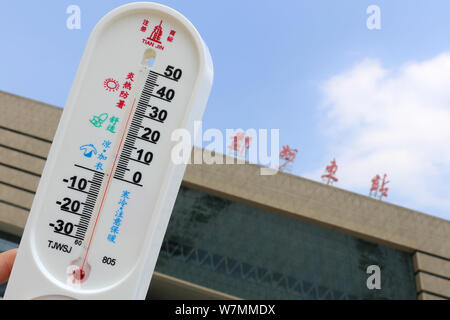 Un residente locale visualizza un termometro che mostra la temperatura attuale arrivano fino a 36 gradi Celsius in un bruciante giorno di fronte al Zhengzhou Est Foto Stock