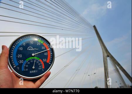 Un residente locale visualizza un termometro che mostra la temperatura attuale di raggiungere 38 gradi Celsius in un bruciante giorno di fronte al Sanxianzhou BRI Foto Stock