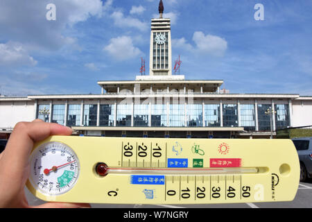 Un residente locale visualizza un termometro che mostra la temperatura attuale di raggiungere 38 gradi Celsius in un bruciante giorno di fronte al Changsha Railwa Foto Stock