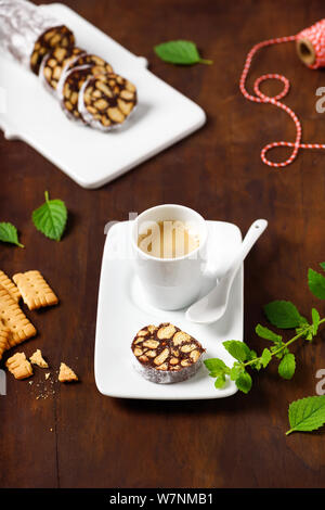 In casa il salame di cioccolato i biscotti con la tazzina di caffè in legno rustico sfondo. Foto Stock