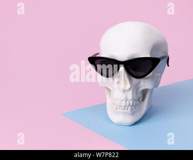 Cranio in occhiali da sole sul rosa pastello sfondo. Costume di Halloween party concept Foto Stock