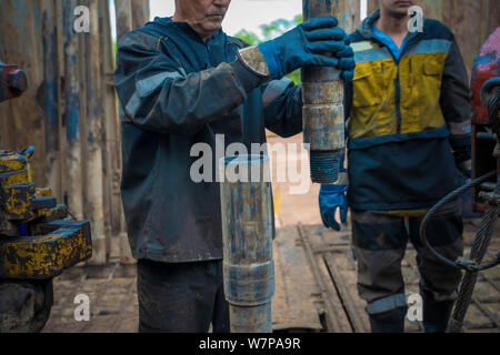 Offshore Oil Rig lavoratore Preparare utensili e attrezzature per la perforazione di pozzi petroliferi e di gas a testa pozzo piattaforma. Che compongono un tubo di trivella il collegamento. Una vista fo Foto Stock