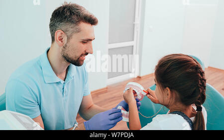 Dentista insegnamento poco razza mista ragazza spazzolare i denti utilizzando denti umani modello presso la clinica dentale Foto Stock