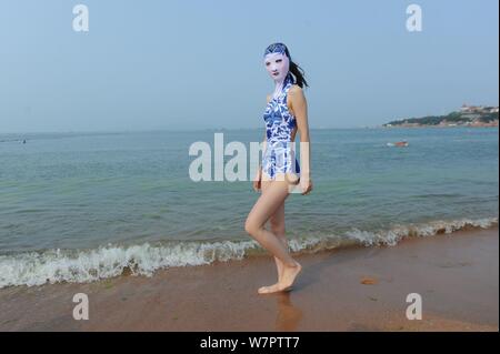 Un modello che indossa un costume da bagno facekini dotate di blu e bianco porcellana e ricamo è raffigurato in un villaggio su una spiaggia di Qingdao City, est della Cina di Shan Foto Stock