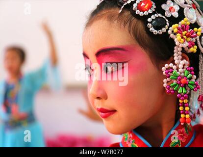 Un pupillo da Binhe scuola primaria termina la sua elaborata Pingju o Ping Opera di costumi e di copricapi con l aiuto di un cinese Opera artista prima di tak Foto Stock