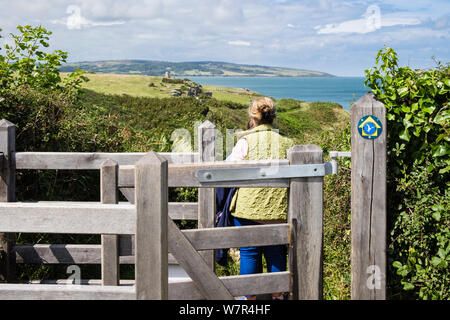 Walker escursioni attraverso un bacio porta sul Galles sentiero costiero con vista della costa. Moelfre, Isola di Anglesey, Galles, Regno Unito, Gran Bretagna Foto Stock