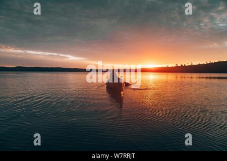 Bellissimo scatto lontano di una femmina in kayak in mezzo di un lago durante il tramonto Foto Stock