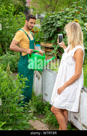 Uomo bello fiori di irrigazione in giardino mentre la donna a scattare foto Foto Stock