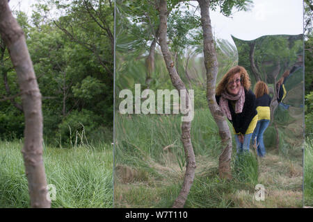 Donna che guarda in 'gigante funhouse" specchio nella foresta, Sculture pubbliche da Rob Mullholland, Port Saint Louis du Rhone, Camargue, Francia, Maggio 2013. Solo uso editoriale. Credit Jean Roche / Le Citron Jaune / Mullholland Foto Stock