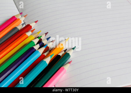 Matite colorate giacciono su un notebook a strisce. Vi è un posto per il testo. Matite colorate sono mostrati in close-up. Presto a scuola. Disegnare con le matite in un n. Foto Stock