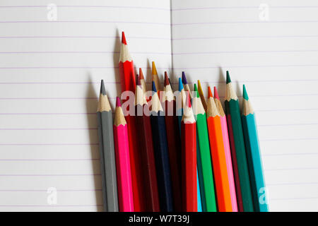 Matite colorate giacciono su un notebook a strisce. Vi è un posto per il testo. Matite colorate sono mostrati in close-up. Presto a scuola. Disegnare con le matite in un n. Foto Stock