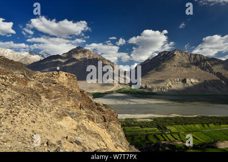 Vista sulla valle di Wakhan nel Pamir mountain, turistico in piedi sulle rovine del Yamchun Fort cercando sul bianco Hindu Kush gamma in Afghanistan, T Foto Stock