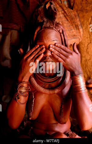 Donna Himba applicando Otjize (una miscela di burro, ocra e ceneri) per la sua pelle, Kaokoland, Namibia, settembre 2013. Foto Stock