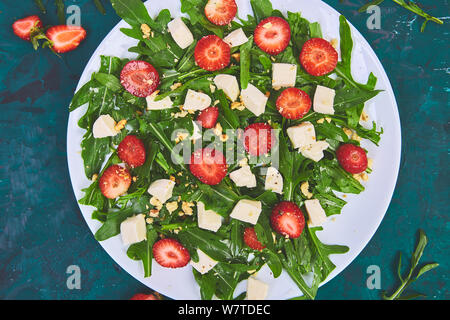 Insalata fresca con rucola, fragole, il formaggio feta e i dadi su sfondo verde. Vegetariano. La dieta alimentare. Il cibo italiano. Vista dall'alto. Copia dello spazio. Foto Stock