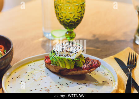 Grano intero sandwich di pane fritto con uovo di quaglia, avocado, erbe e semi su sfondo nero. Pulire mangiare sano colazione vegan. Foto Stock