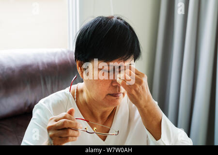 Vecchia donna rimozione degli occhiali, massaggiare gli occhi dopo la lettura di un libro cartaceo. provare disagio a causa della lunga indossando occhiali, affetti da occhi Foto Stock