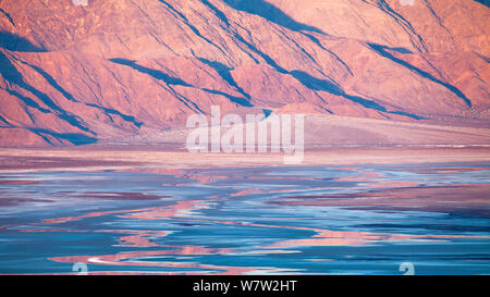 La mattina presto su montagne distanti, creando vibranti riflessi nelle saline del Parco Nazionale della Valle della Morte, California, USA, dicembre 2013. Foto Stock