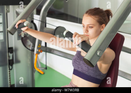 Giovane bella bionda ragazza sportiva non cassa della macchina premere esercizio in palestra Foto Stock