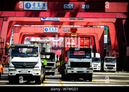 Una gru ponti sollevatori di veicoli contenitori per essere spediti all'estero da parte dei camion su una banchina del porto di Qingdao nella città di Qingdao, Cina orientale della provincia di Shandong, 13 Foto Stock