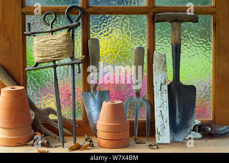 Potting Shed finestra con vasi di fiori, lato forche, stringa e cazzuola sul davanzale. Foto Stock