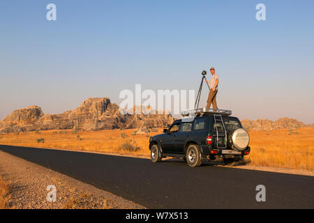 Wildlife Photographer Ingo Arndt sulla assegnazione per una migrazione di locusta story, in piedi sul tetto da 4WD di scattare le foto. Isalo National Park, Madagascar. Agosto 2013. Foto Stock