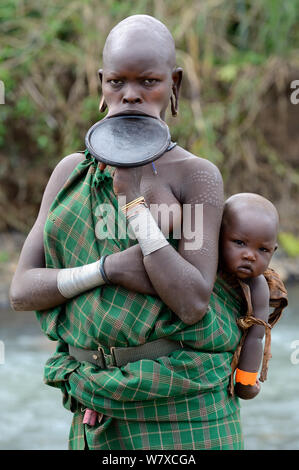 Ritratto di Suri / Surma donna che indossa la piastra a labbro e portando il suo bambino. Omo river Valley, Etiopia, settembre 2014. Foto Stock