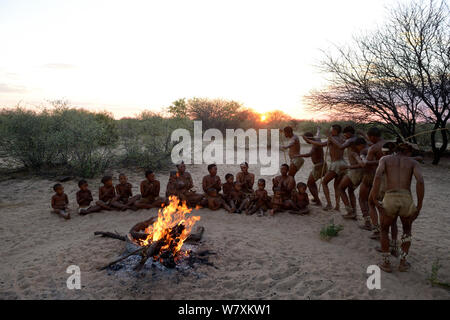 Naro Boscimani San famiglia, gli uomini di eseguire la tradizionale danza e donne che cantano e seduti intorno al fuoco all'alba. Kalahari Ghanzi regione, Botswana, Africa. La stagione secca, ottobre 2014. Foto Stock