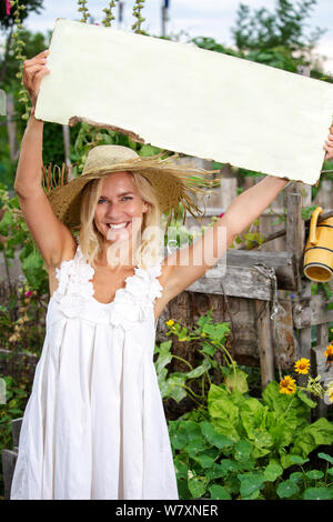 Bella donna bionda in piedi in giardino e tenendo un cartello in legno Foto Stock