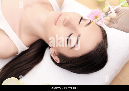 Stretta di mano di esperti estetista iniettare nelle femmine di fronte. La donna chiuse gli occhi con gioia. Lei è dolcemente sorridente Foto Stock