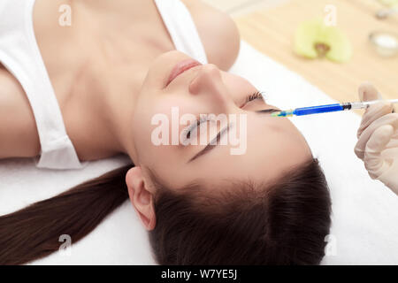 Stretta di mano di esperti estetista iniettare botox nelle femmine di fronte. La donna chiuse gli occhi con gioia. Lei è dolcemente sorridente Foto Stock