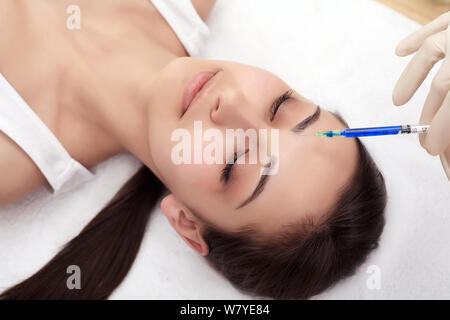 Stretta di mano di esperti estetista iniettare nelle femmine di fronte. La donna chiuse gli occhi con gioia. Lei è dolcemente sorridente Foto Stock