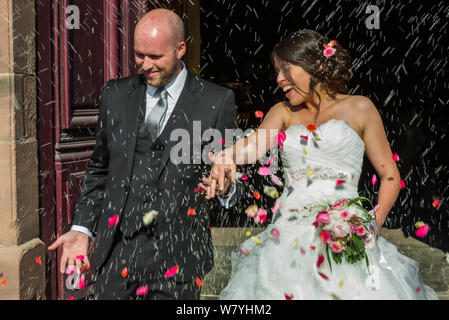 La gente buttare il riso e petali di fiori sul sposi novelli wile lasciano la chiesa Foto Stock