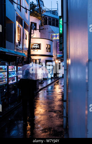 Un uomo che tiene l'ombrello cammina lungo una strada piovosa a Tokyo, Giappone Foto Stock