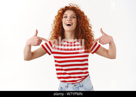 Orgogliosa magniloquente bella assertivo giovani redhead curly donna sorridente fiducioso puntando se stessa raffreddare la vanteria possiedono le realizzazioni Realizzazione stand Foto Stock