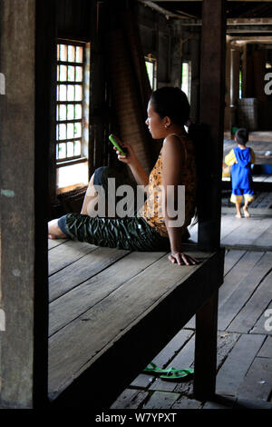 Dayak donna sul telefono cellulare, in longhouse, Pontianka, West Kalimantan, Borneo Indonesiano. Giugno 2010. Foto Stock