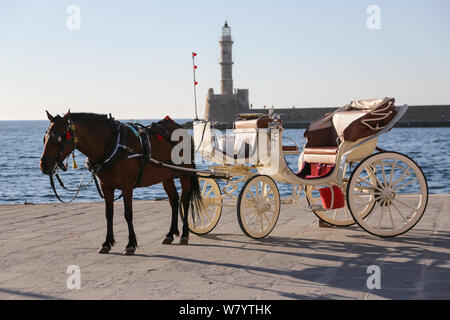 Una vista generale di una carrozza trainata da cavalli nella parte anteriore del XVI secolo faro al vecchio porto veneziano, nella città di Chania, Creta, Grecia Foto Stock