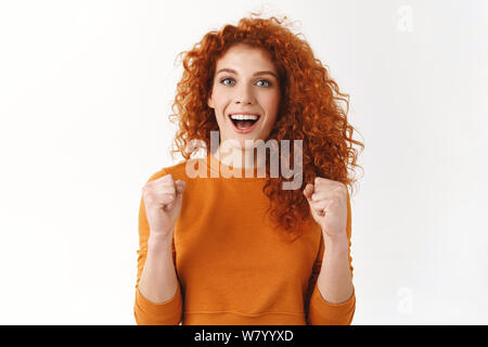 Emozionato gorgeous redhead ragazza radicamento per squadra preferita. Curly ragazza stringono i pugni motivato ed ambizioso, sorridente largamente, tifo, trionfante Foto Stock