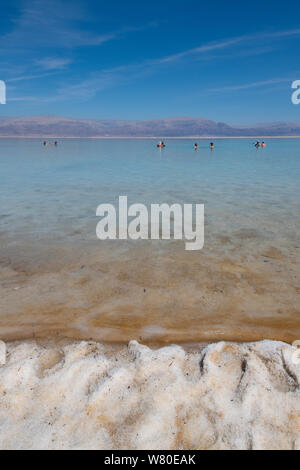 Israele, il Mar Morto. Il luogo più basso in tutto il mondo in oltre 400 metri sotto il livello del mare. Salty Beach vista con i turisti galleggianti in distanza. Foto Stock