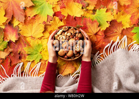 Autunno laici piana. Donna mani ciotola di legno con un misto di dadi. Cibo sano e snack. Vegano vegetariano, farina cruda concetto. Noci, mandorle, hazeln Foto Stock