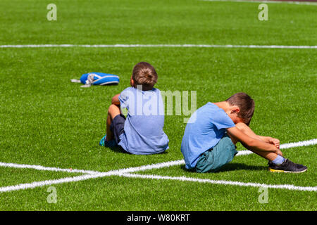 Due triste deluso ragazzi seduta di schiena sul prato di Stadium Foto Stock