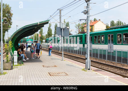 Persone in attesa alla stazione Kaszasdulo di Budapest Ferroviario di Interesse Locale HEV con due treni provenienti da direzioni opposte a Budapest, Ungheria Foto Stock