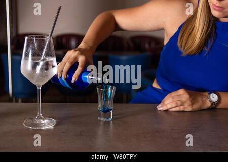 Ragazza fa di una laguna blu cocktail sul bar nel ristorante. Donna blu di versare il liquido da una bottiglia in un bicchiere piccolo. Bere alcool concept Foto Stock