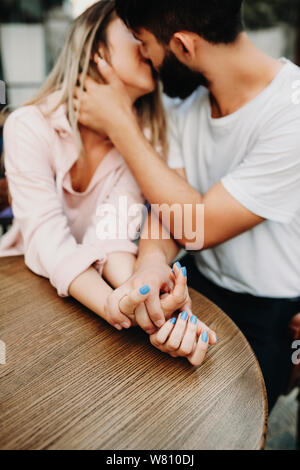 Tenere la mani di una coppia adorabile abbracciando e baciando seduti al ristorante esterno. Foto Stock