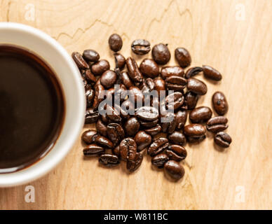 Alta angolazione di un mucchio di chicchi di caffè e un pieno per metà tazza da caffè Foto Stock