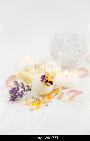 Bellissimo set con messa a fuoco selettiva su bianco cremoso idratante bagno piccola bomba a sfera con fiore secco petali di fiore, spa candele accese e flowe secco Foto Stock