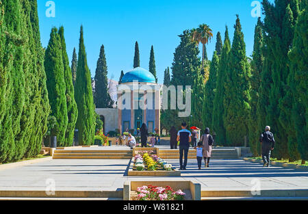 SHIRAZ, IRAN - 14 ottobre 2017: la gente a piedi il viale di cipressi di tomba Saadi (mausoleo dei Sa'di, Sadiyeh) con letto di fiori in mezzo alla strada e riccamente dec Foto Stock