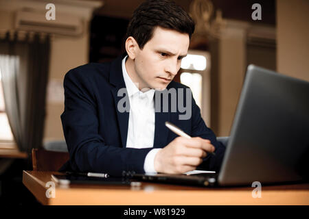 Close up di un giovane imprenditore caucasico lavorando nel suo ufficio mentre guardando il suo computer portatile sul serio. Foto Stock