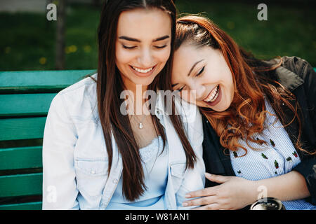 Close up ritratto di due fantastici fidanzate divertirsi al di fuori su un banco mentre la ragazza con i capelli rossi sta appoggiando la sua testa sulla sua fidanzata della spalla di l Foto Stock