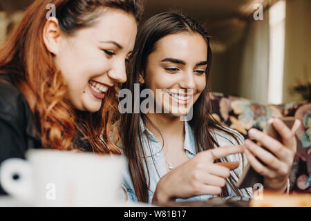 Ritratto di una bella donna che guarda uno smartphone a sorridere insieme con la sua ragazza con i capelli rossi pur avendo un buon tempo in una caffetteria. Foto Stock